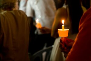 Closeup of people holding candle vigil in dark seeking hope