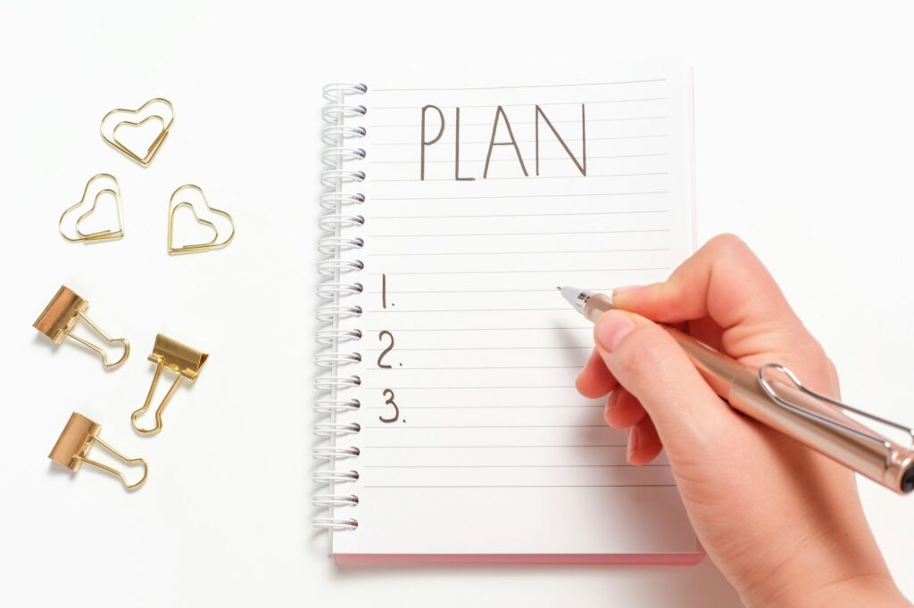 Female hand writes plan in a notebook on white background close-up.